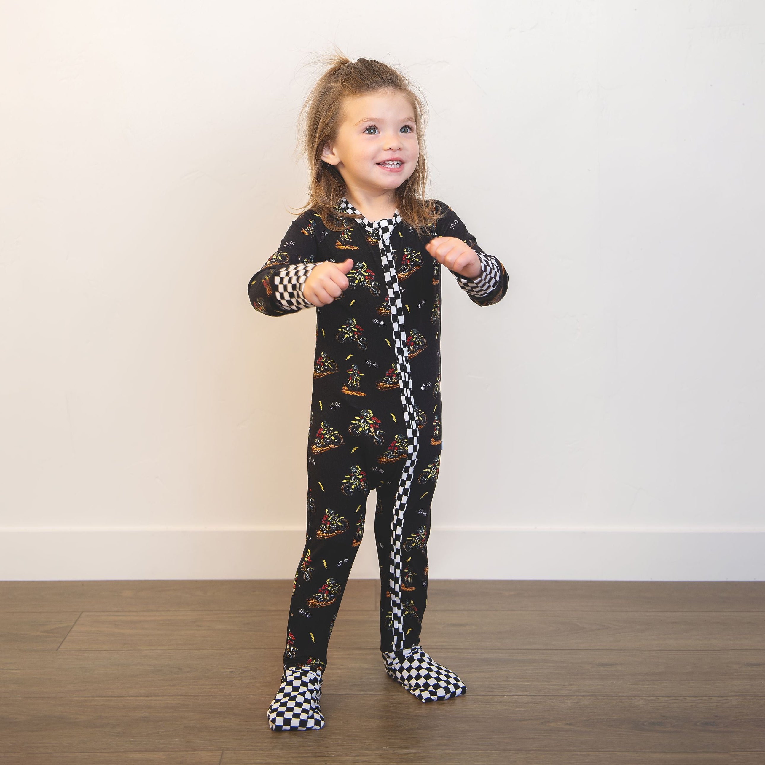 Child wearing a black onesie with motopatterns on a plain background
